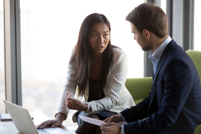 an Asian woman and a Caucasian man are sitting on a couch discussing important business